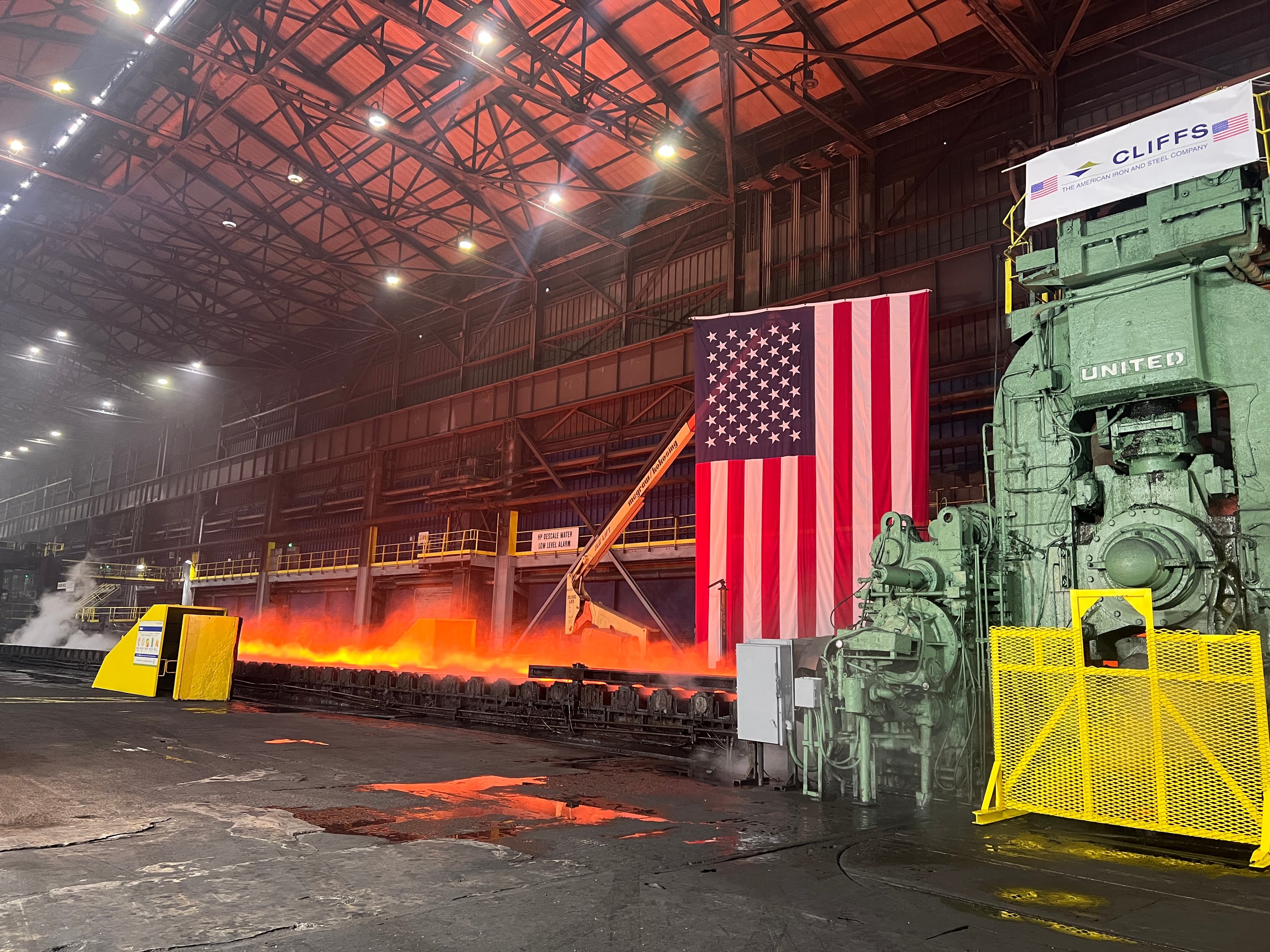 Glowing steel on a production line beneath an American flag at Cleveland-Cliffs in Middletown, Ohio